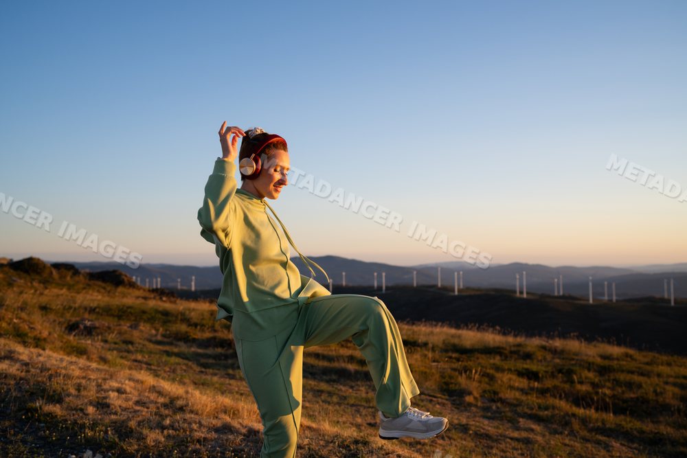 A white woman dances to music outdoors at sunset in Galicia, Spain