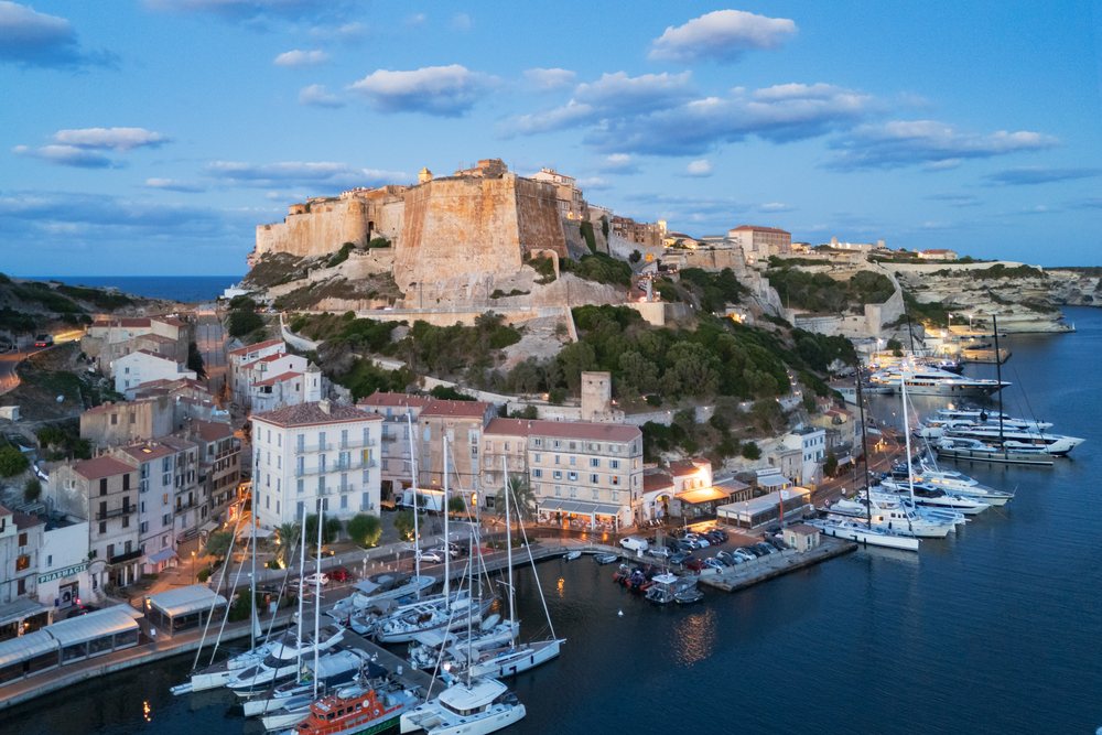 Fortified Citadel on a hilltop overlooking harbor with moored boats, waterfront residential buildings, and sea at dawn, Travel Photography, Bonifacio, Corsica, France.