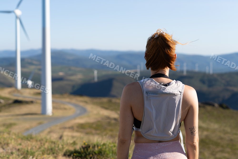 A white woman with a backpack observes wind turbines