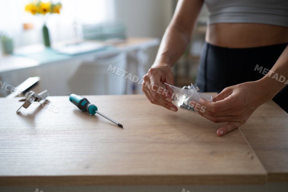 A white person assembling wooden furniture by unpacking screws