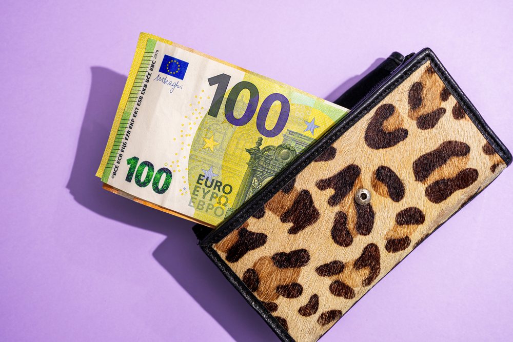 100 Euro banknote partially inside a leopard print wallet on a purple studio background, Studio Shot.