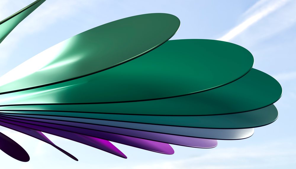 Abstract outdoor metal sculpture features large overlapping colored petals reflecting sunlight against a clear blue sky.