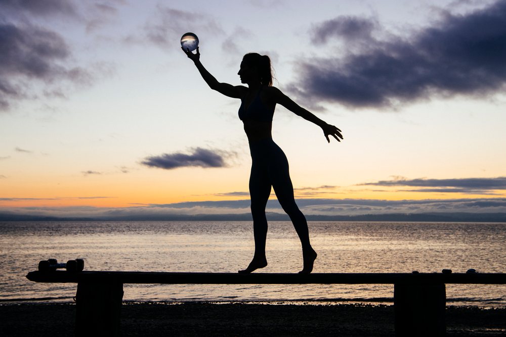 Silhouette of a barefoot woman balancing on a beam by the ocean at sunset, WA, USA.