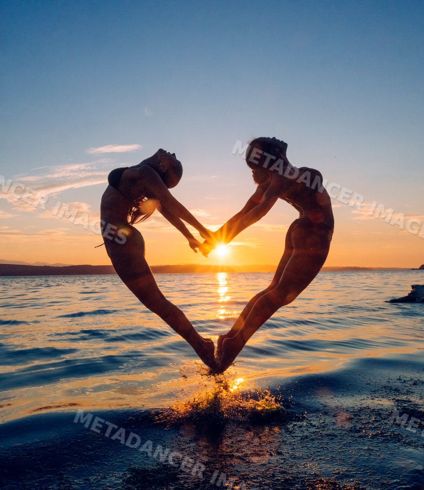 Two women practice partner acrobatics yoga at sunset by the water