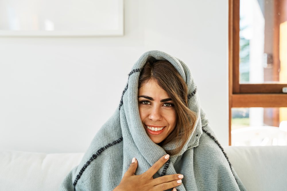 A white woman wrapped in a blanket smiles warmly indoors