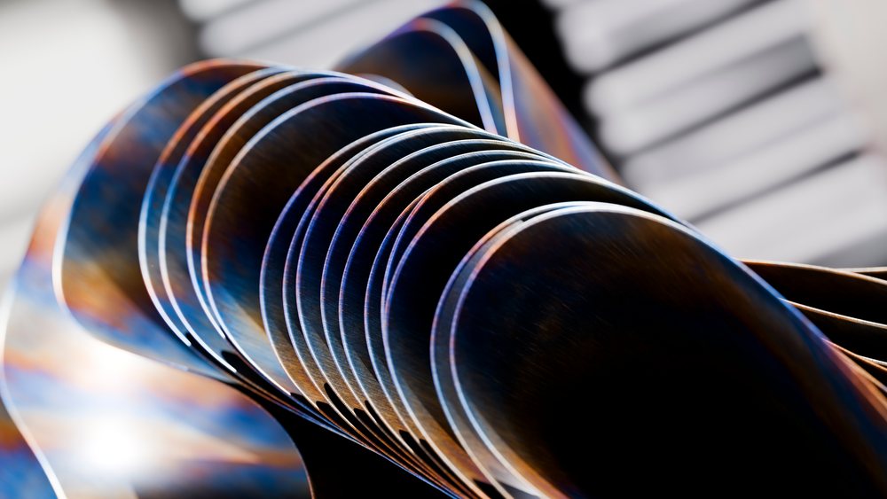 Metal spoons arranged in a row displaying curved bowls with reflections and a blurred background.