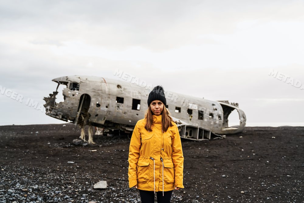 A white woman stands near a crashed airplane wreckage in Iceland's