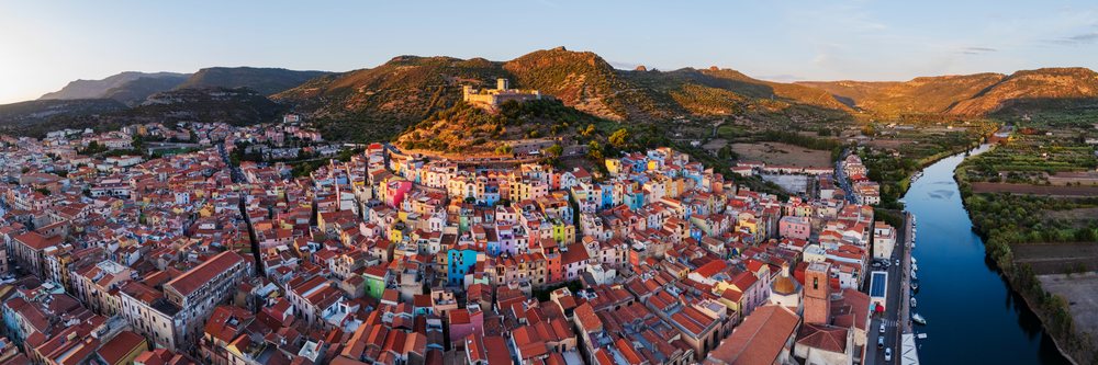 Sunset view of Bosa Old Town with colorful houses, hilltop castle, river with boats, and mountainous landscape, Travel Images, Sardinia, Italy.