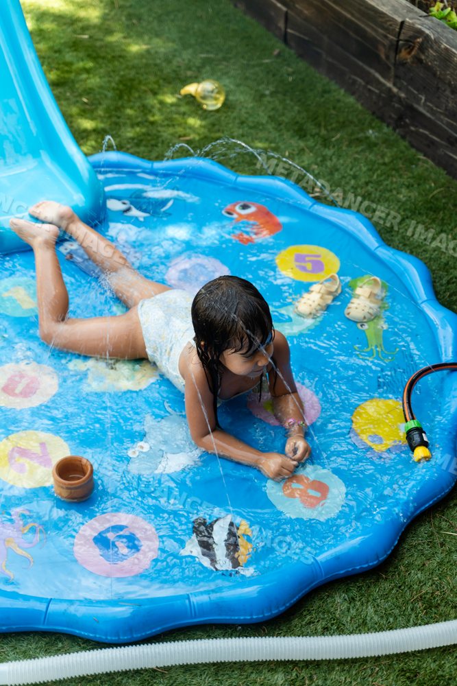 White Child playing on inflatable splash pad with water sprays