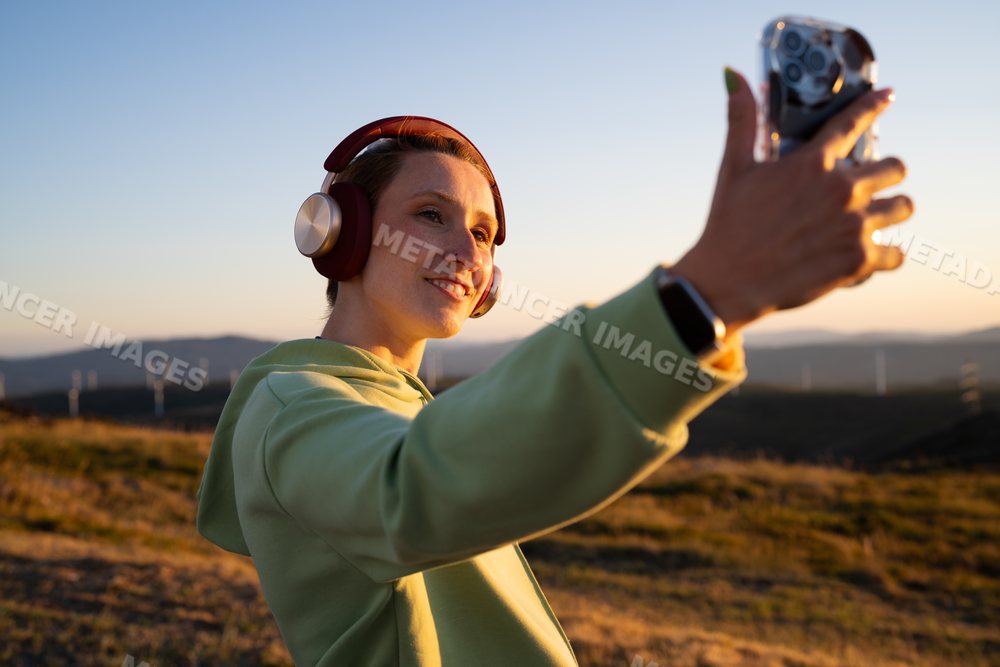 Young white woman takes a selfie with headphones on outdoors