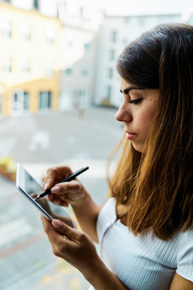 A woman uses a stylus pen on a tablet indoors in a hotel