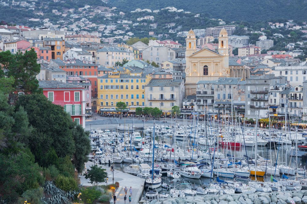 Numerous sailboats docked in Bastia harbor with historic waterfront buildings and a central church at dusk, Travel Photography, Corsica, France.