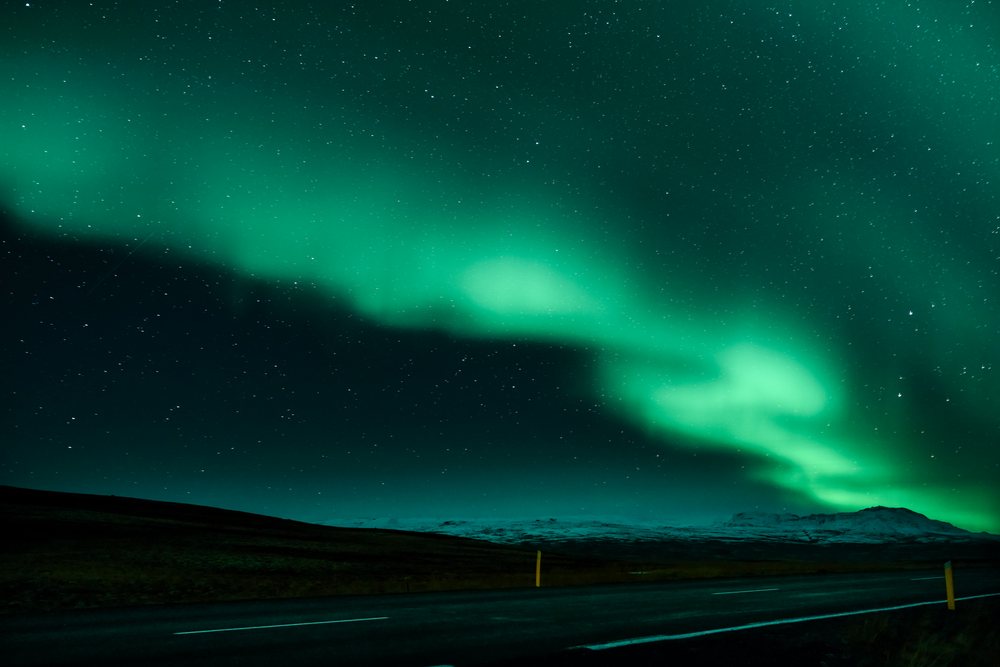 Green aurora borealis lights illuminate a mountain road