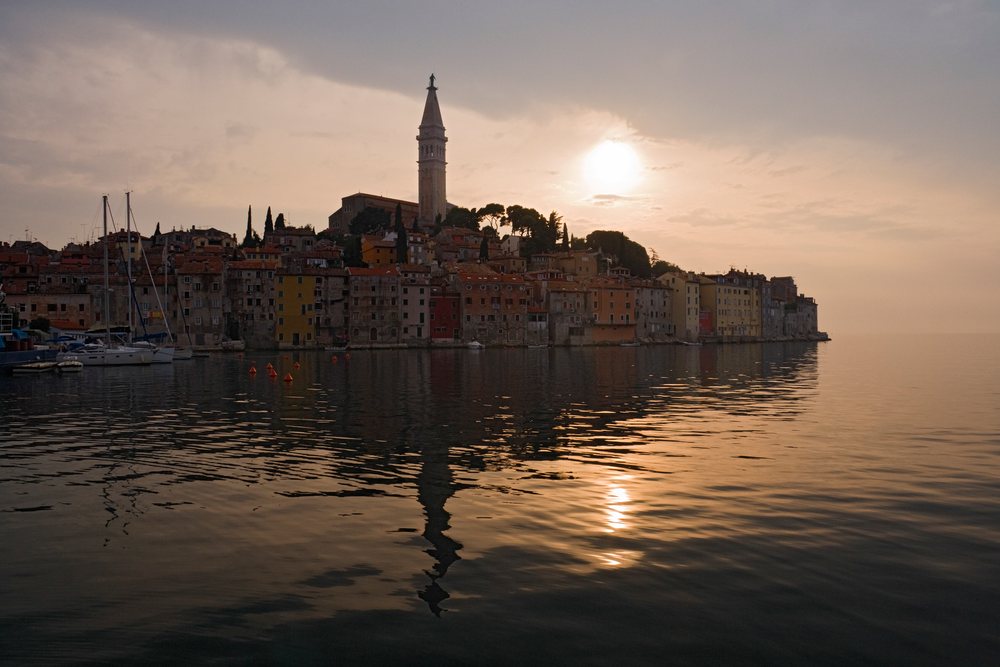 The coastal town of Rovinj with its church tower reflects on calm water, Sunset, Croatia.