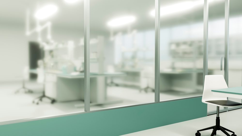 Modern laboratory featuring a glass wall partition and white chair within a sterile scientific workspace.