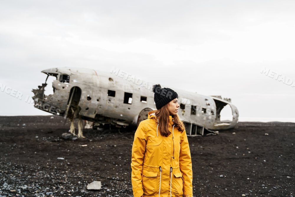 A white woman stands by an abandoned aircraft wreck on Iceland's