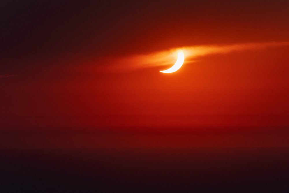 Crescent of solar eclipse visible through clouds with red sky over, Landscape, Lifestyle, Valldemossa, Mallorca, Spain.