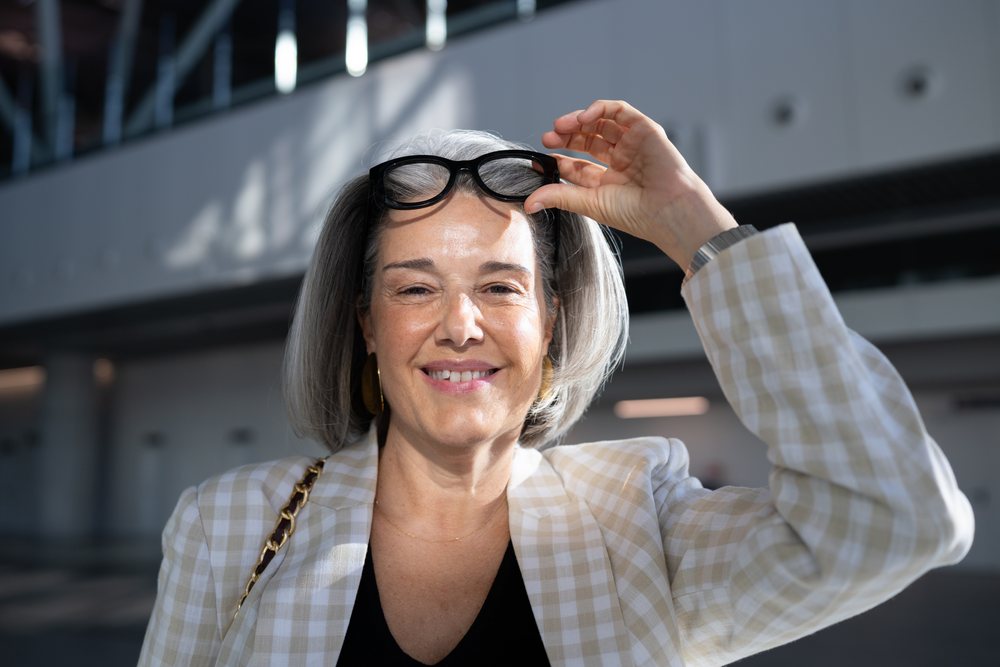 Mature woman in a plaid blazer and black eyeglasses smiles while raising her glasses indoors, businesswoman, Spain, Madrid.