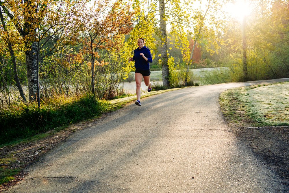 Woman running on a paved path in a park during a sunny morning, Washington, Bainbridge Island, USA.