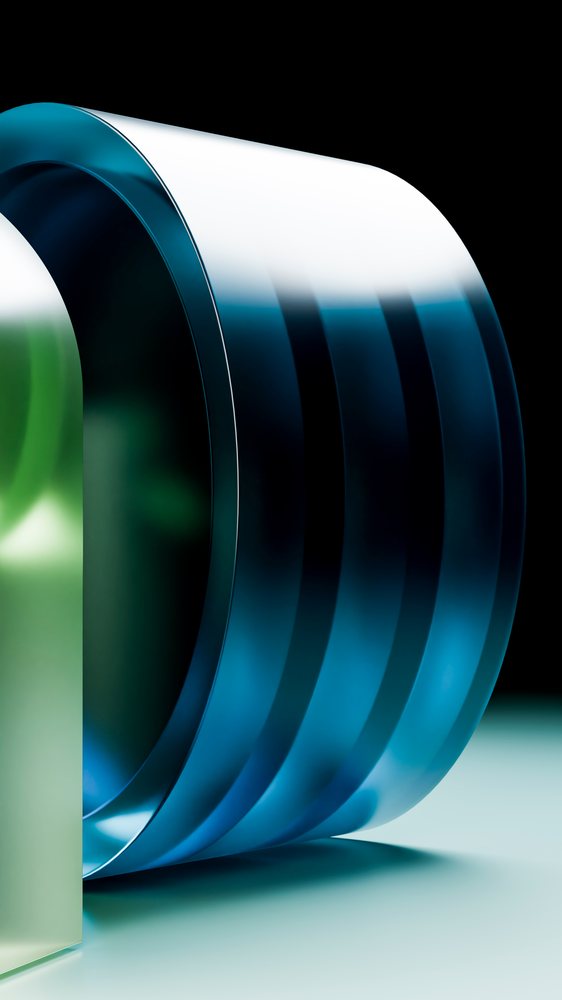 Blue and green curved glass sculpture with a reflective surface displayed under studio lighting against a black background.