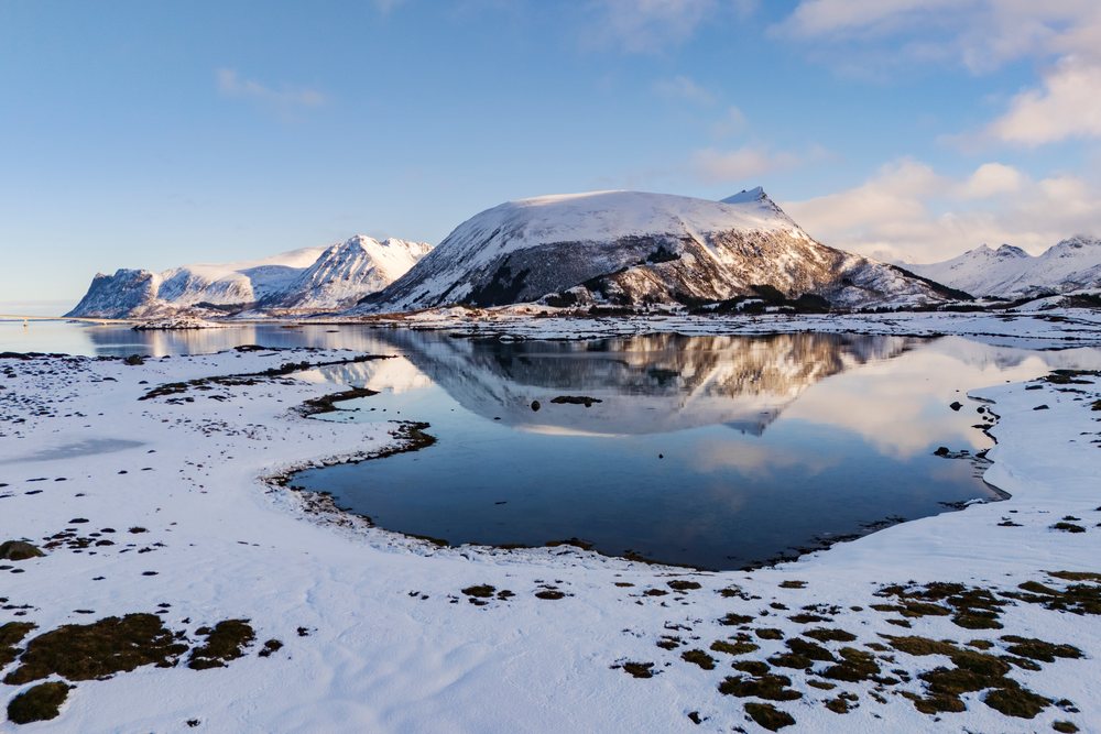 Snow-covered mountains reflect in calm waters of Landmeen Fjord, Arctic, Landscape, Klepstad, Lofoten, Norway.