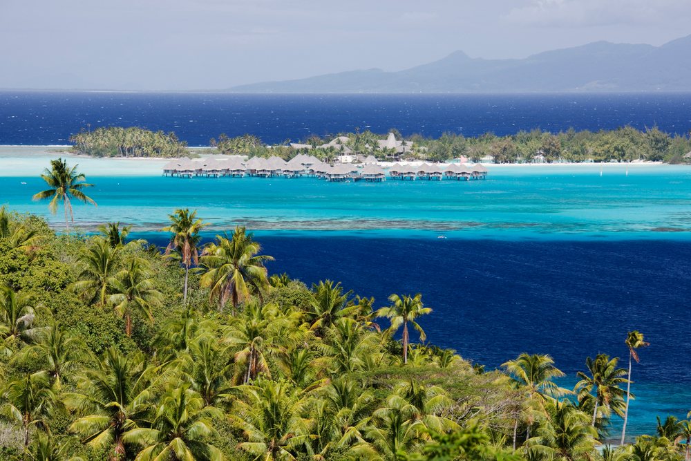 Overwater bungalows at a Bora resort with palm trees and vibrant turquoise lagoon waters, Tahiti, French Polynesia.