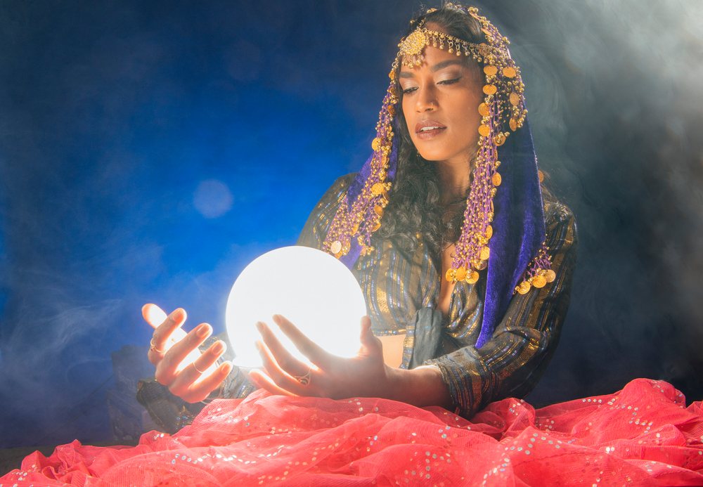 A woman dressed as a mystical figure holding a glowing crystal ball with a smoky dark background in the, fortune teller, spirituality, USA.