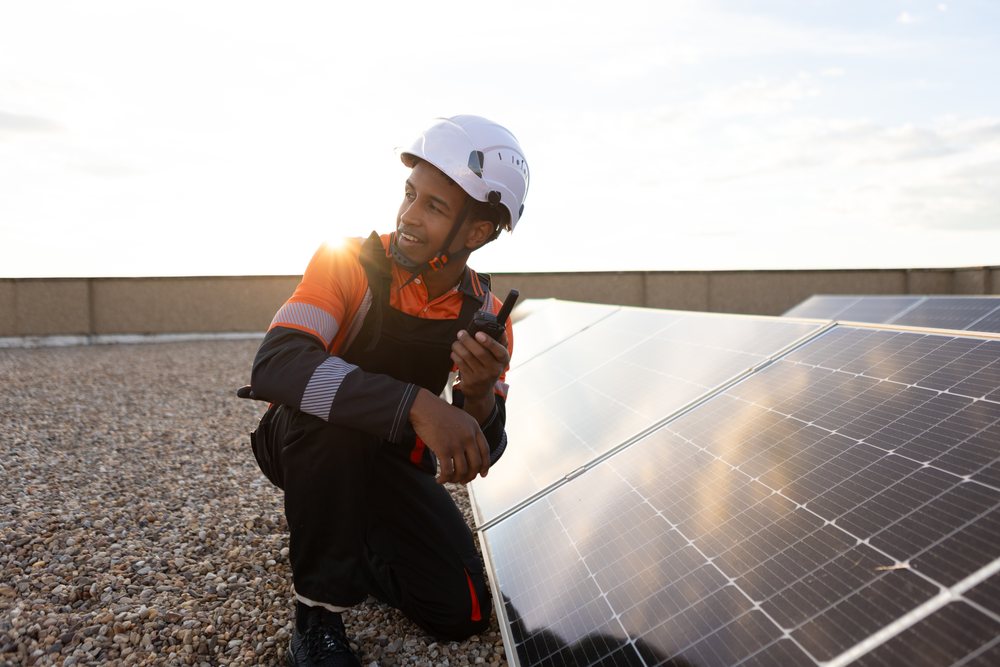 Worker wearing helmet inspects solar panels on a rooftop in Madrid at sunset, ensuring clean energy production, Spain.