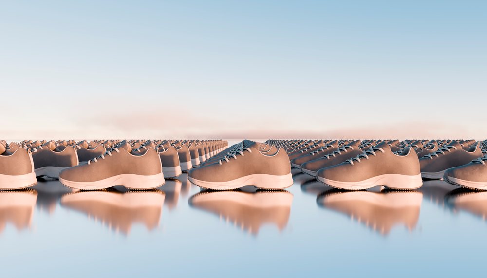 Rows of modern tan sneakers with white soles and laces reflecting on a shiny surface.