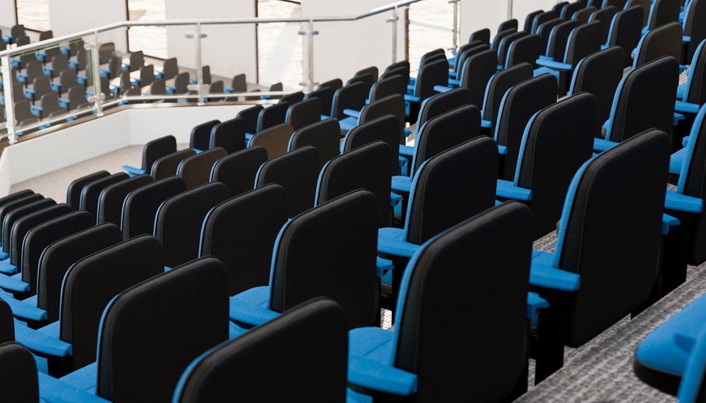Rows of empty blue and black auditorium seats arranged on a staircase inside a modern conference room with glass railing.