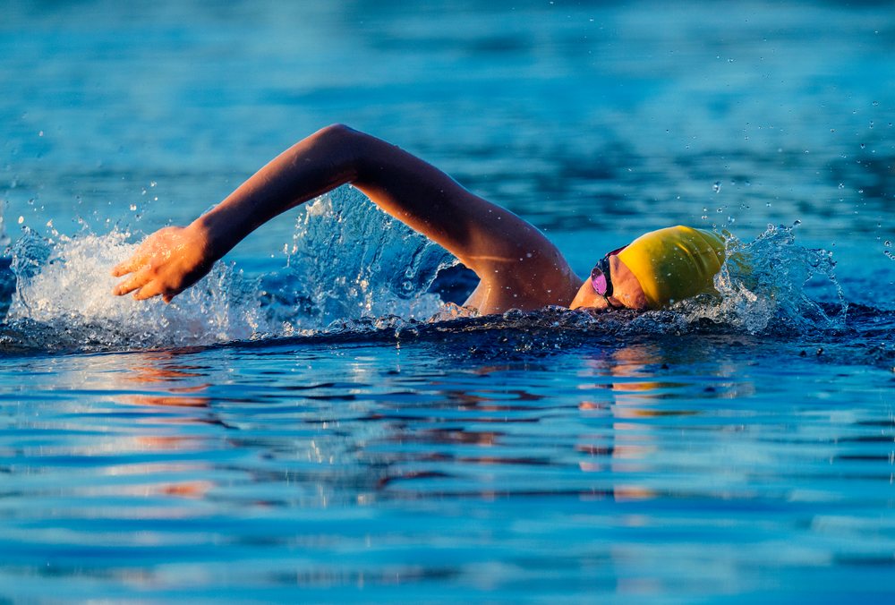 Swimmer performing a freestyle stroke in open water wearing a yellow swim cap and goggles, USA.