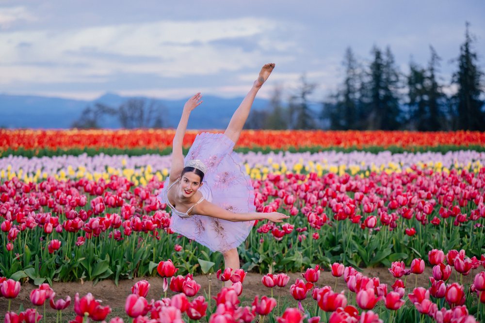 Ballet dancer in a purple tutu striking an elegant pose among colorful tulip fields outdoors, USA.