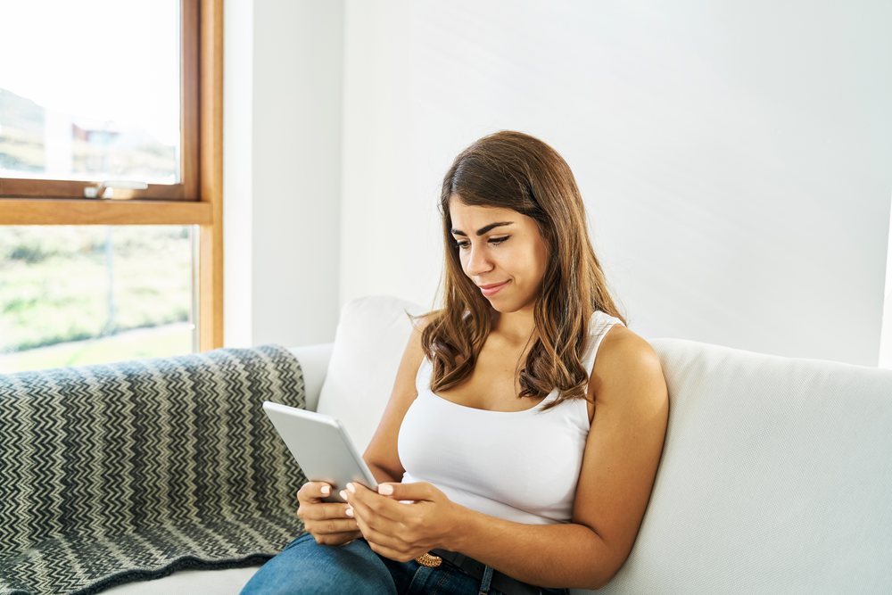 A white woman sitting on a sofa and using a tablet