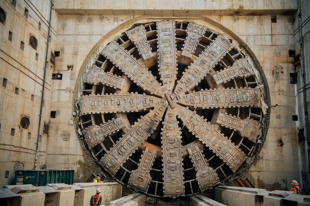 The large circular drill head of a tunnel boring machine used in underground construction is seen with workers inspecting it at a construction site, a tunnel boring machine, drilling, USA.