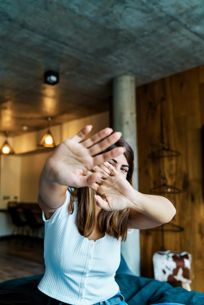A woman playfully covers her face inside a modern cozy room in a hotel