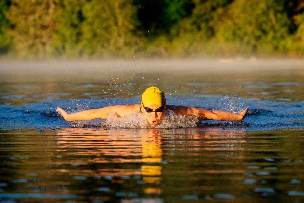 Swimmer performing butterfly stroke in open water during early morning wearing a yellow swim cap and goggles, USA.