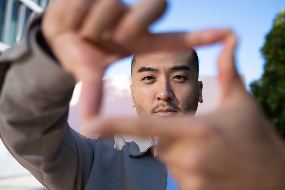 Man outdoors making a rectangular frame with his hands in front of his face under a blue sky in natural daylight, Madrid, Spain.