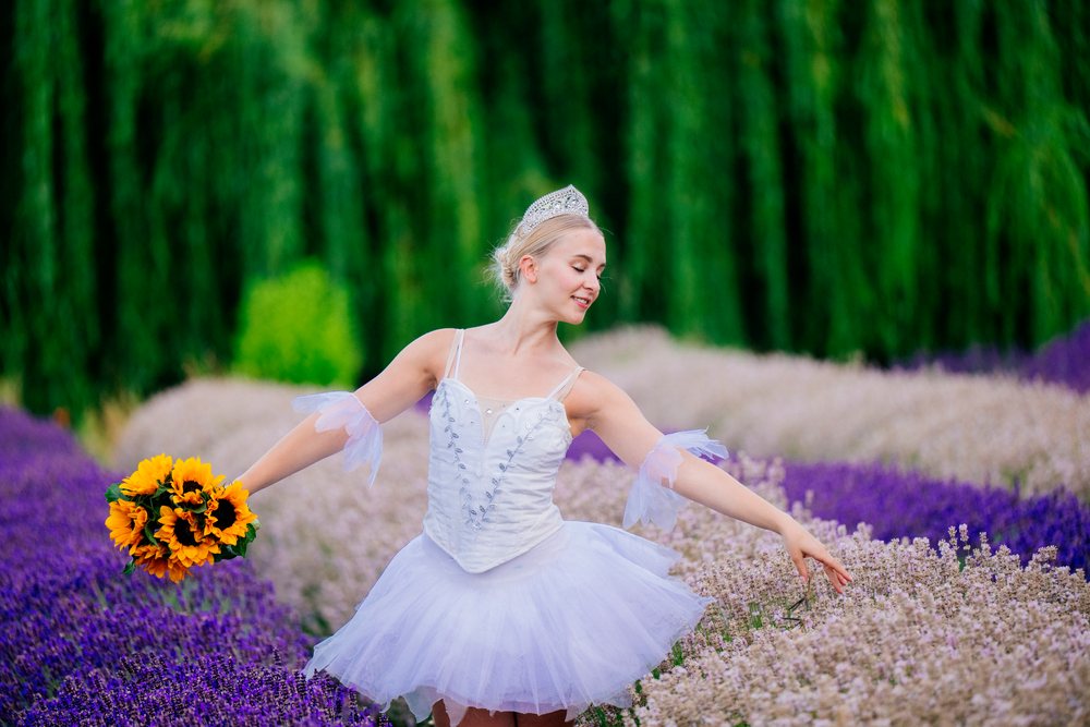 A ballerina in a white tutu and tiara gracefully dances through a colorful lavender and flower field, WA, USA.