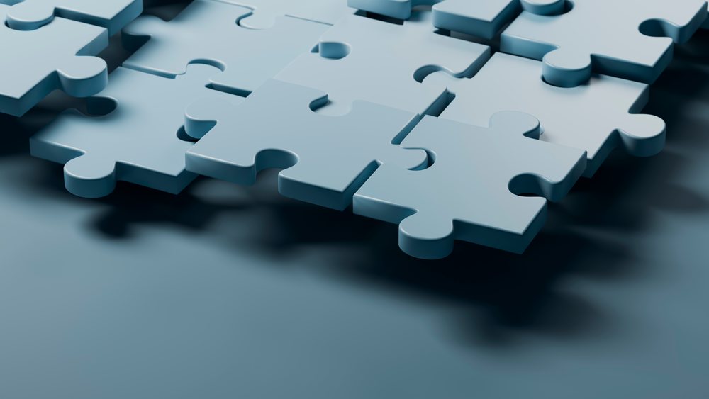 Close-up of blue 3D interlocking puzzle pieces fitting together on a smooth surface in a conceptual abstract arrangement.