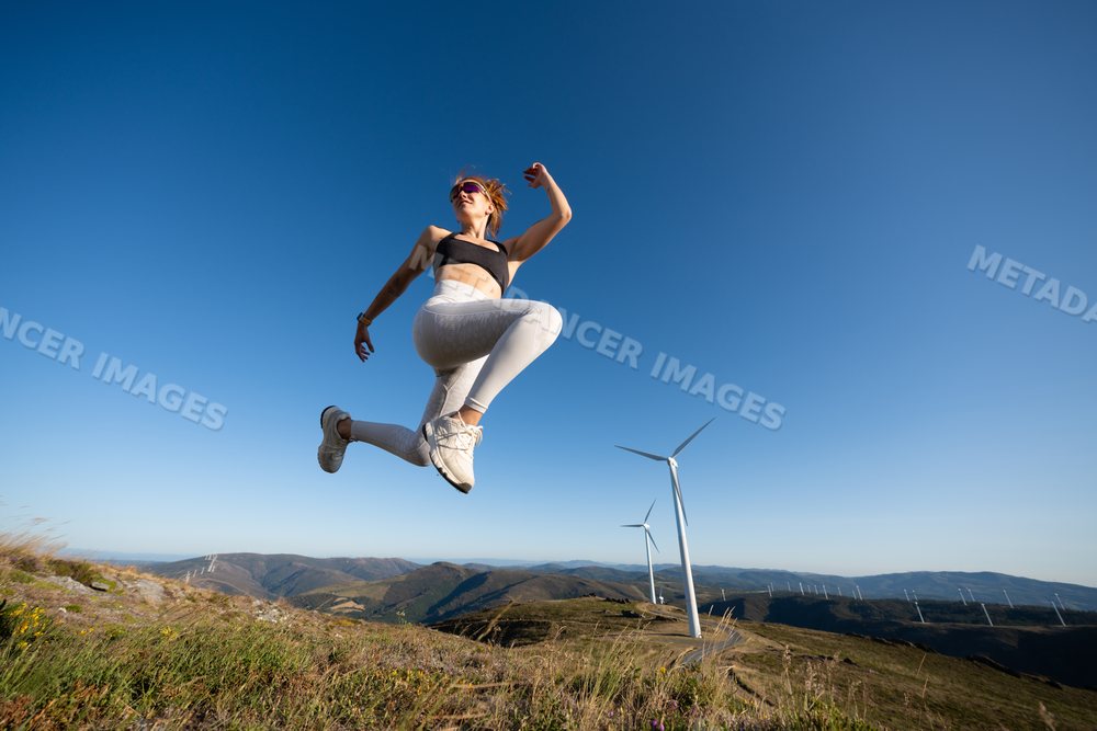 White Woman jumping actively outdoors near wind turbines in Galicia