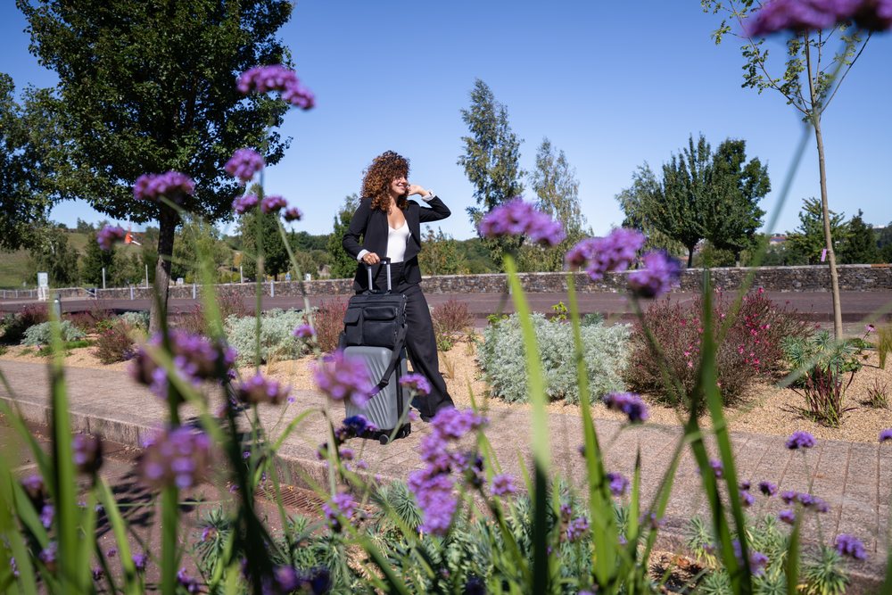 Businesswoman walking with rolling luggage along a garden path, Business Travel, Spain.
