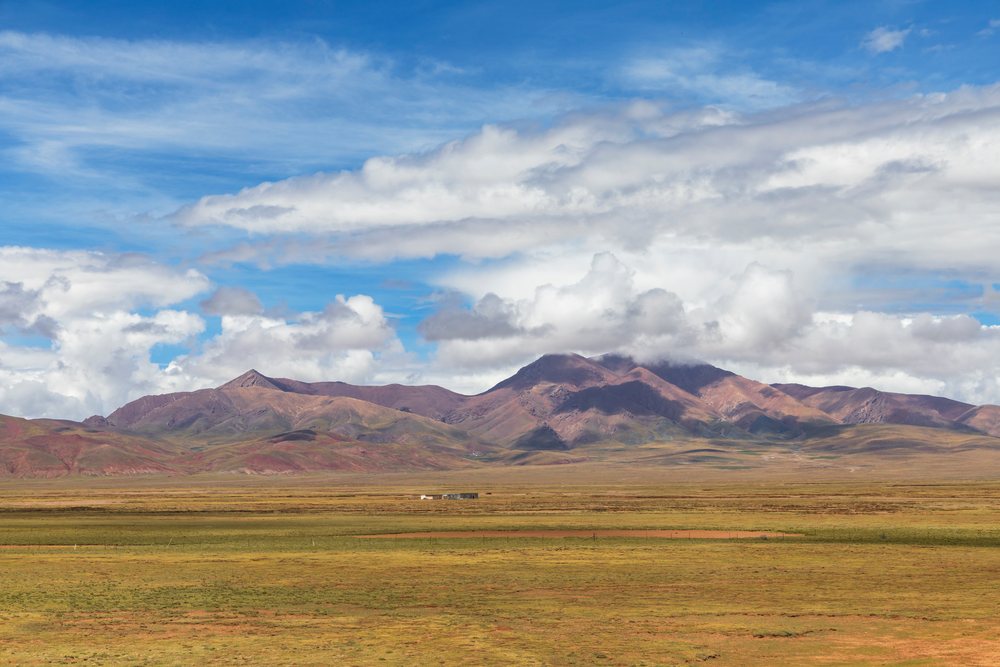 Open plateau landscape featuring expansive grassy plains and mountain ranges under a partly cloudy sky, Kham Tibet, Amdo County, Autonomous Region of Tibet.