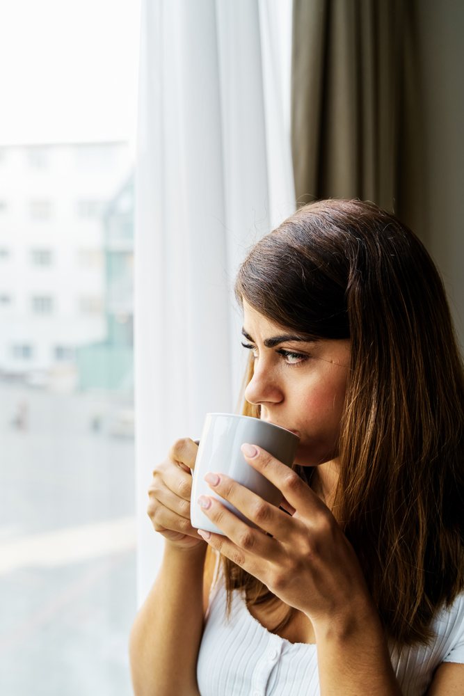 A woman drinks coffee looking out a window in an Iceland apartment