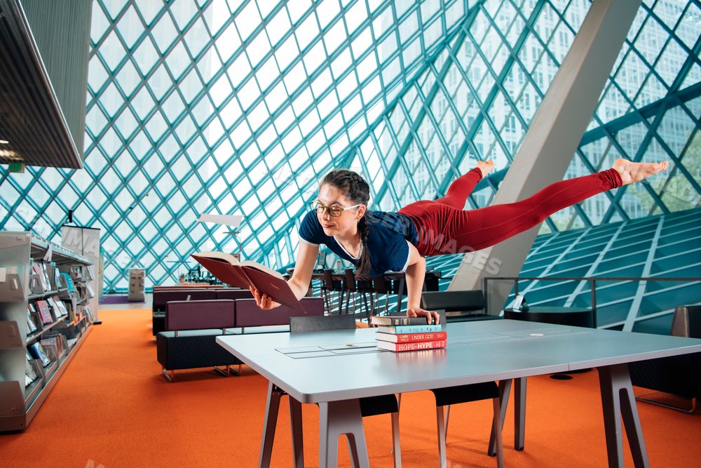 A woman balances and reads a book in a library