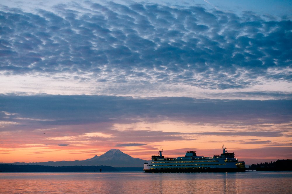 Passenger ferry crossing calm water near Bainbridge Island at sunset with Mount Rainier visible in the background, WA, USA.