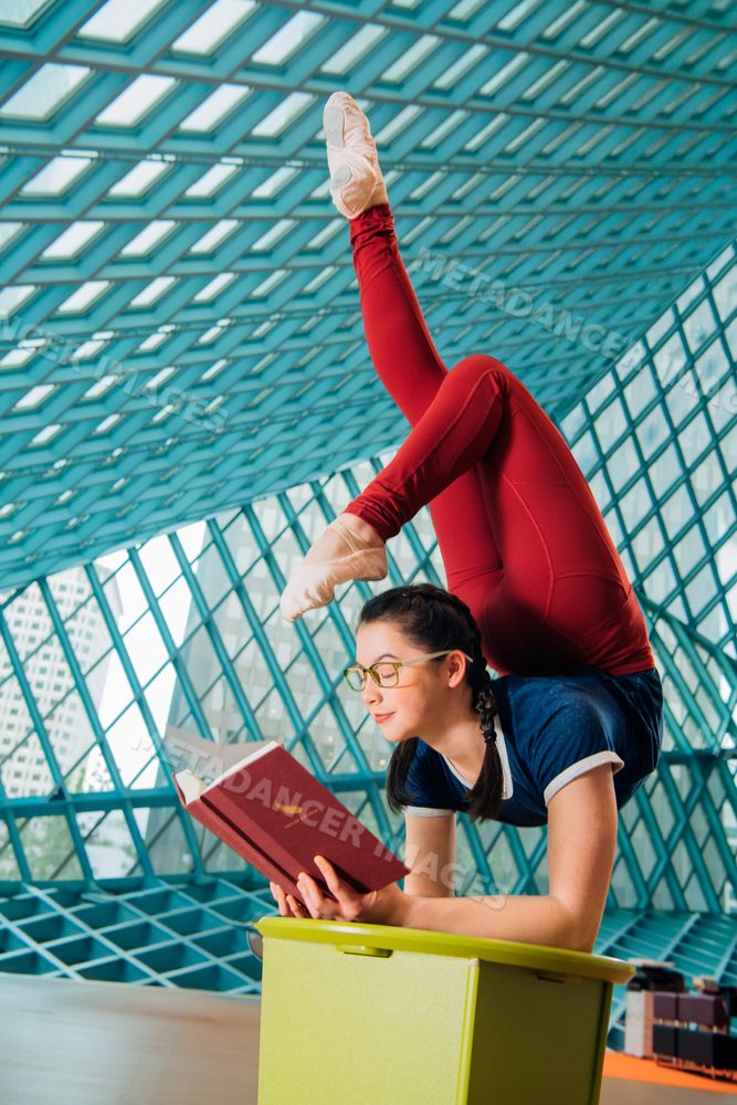 A young woman practices contortion while reading in a library