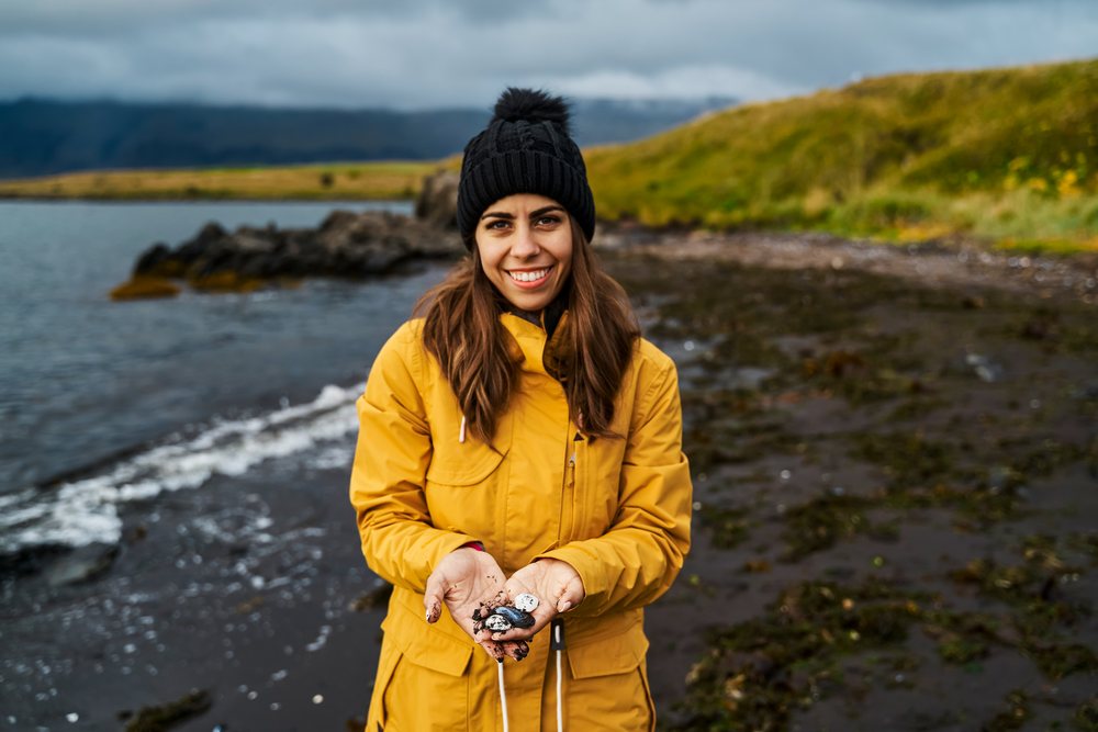 A white woman holding rocks on a black sand beach in a beach