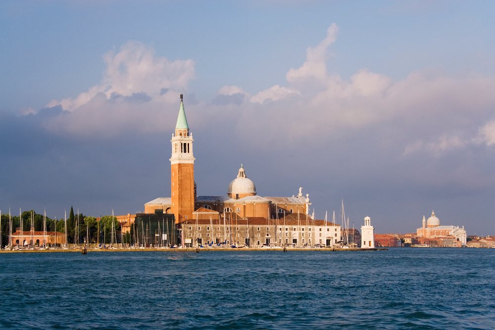 Church of San Giorgio Maggiore with dome and bell tower on a Venetian island waterfront under a partly cloudy sky, Venice, Italy.
