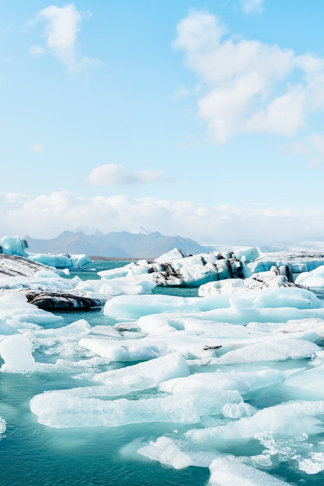 Floating icebergs and glacier ice fill a cold glacial lagoon surrounded by mountainous landscape, Iceland.
