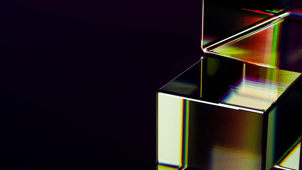 Transparent glass box with open lid reflecting a prism-like colorful light in a minimalist studio setting with dark background.
